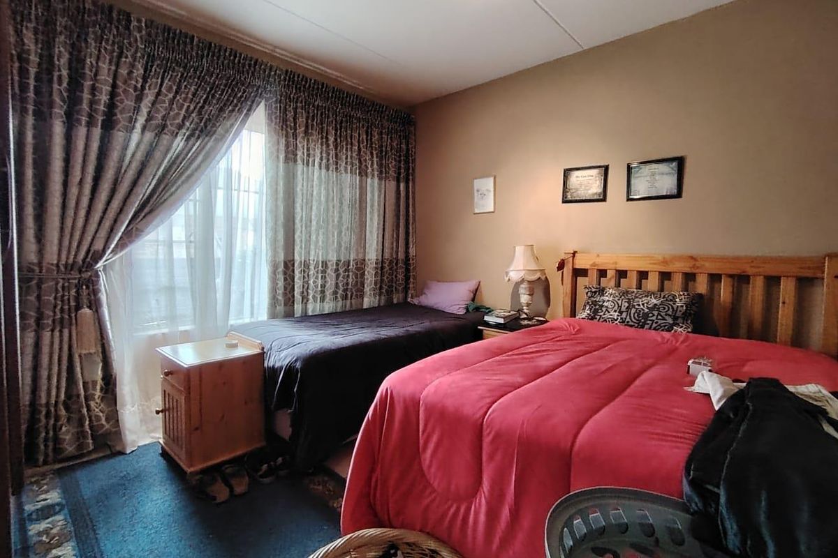 A bedroom featuring a large window with curtains, providing natural light and space for multiple beds.