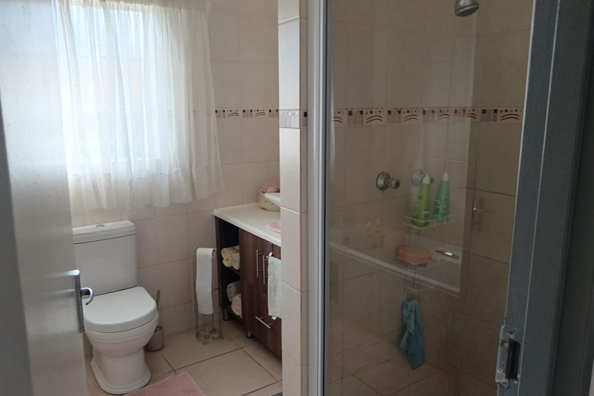 A functional bathroom featuring a glass-enclosed shower, a built-in vanity cabinet, and a standard toilet with neutral wall tiling.