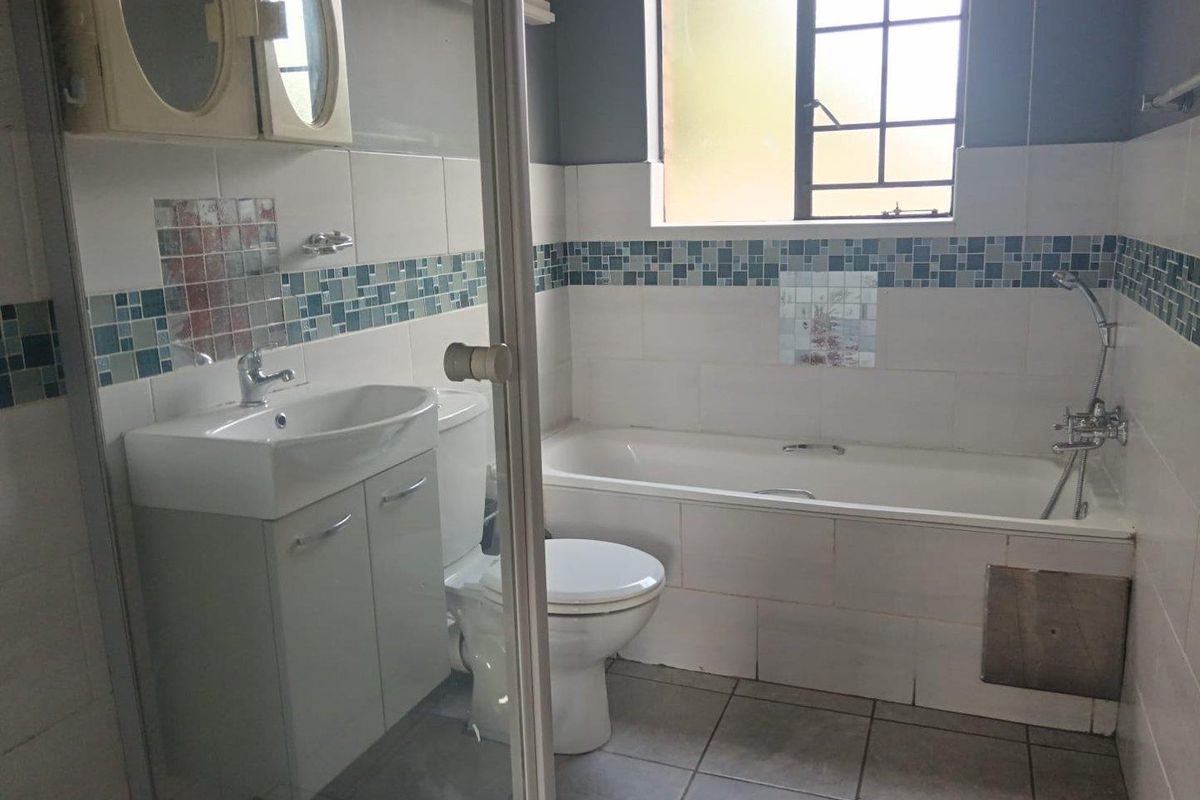 A functional bathroom featuring a built-in bathtub with shower attachment, a vanity basin, and a toilet, finished with tiled walls and flooring.