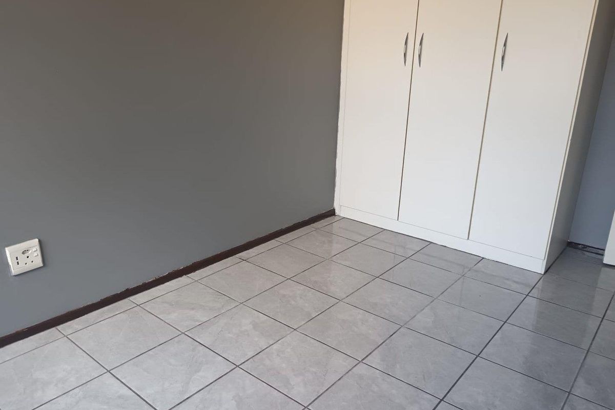 A bedroom featuring light grey tiled flooring, a built-in white wardrobe, and a dark grey accent wall.