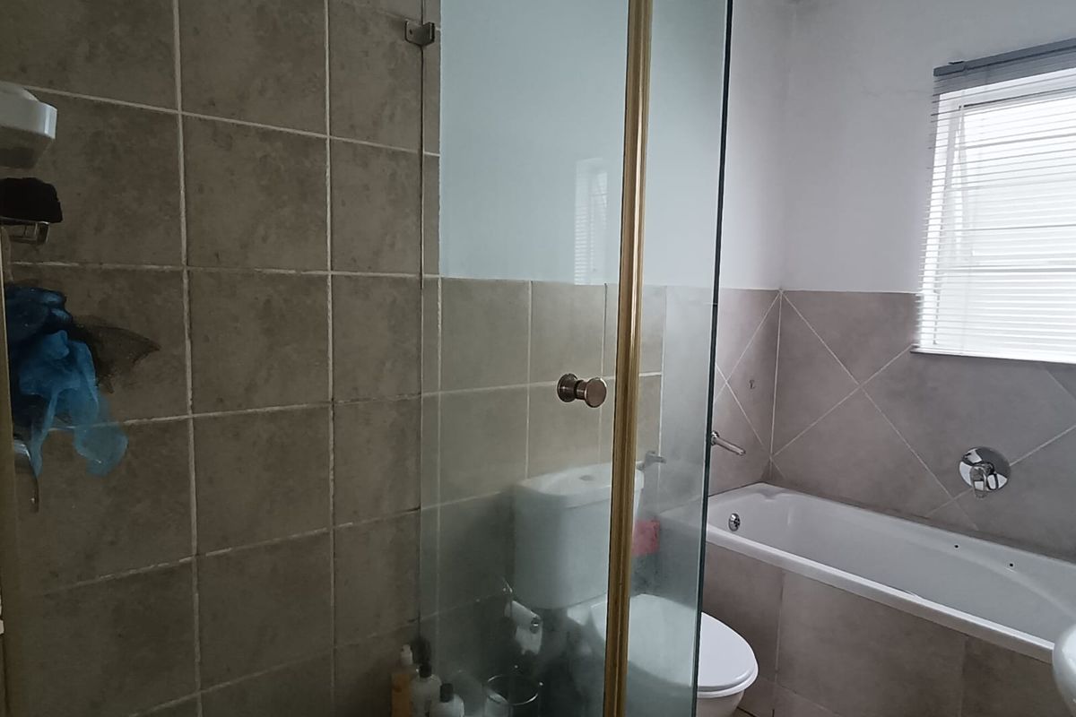 A functional bathroom featuring a glass-enclosed shower, a built-in bathtub, and neutral wall and floor tiling.