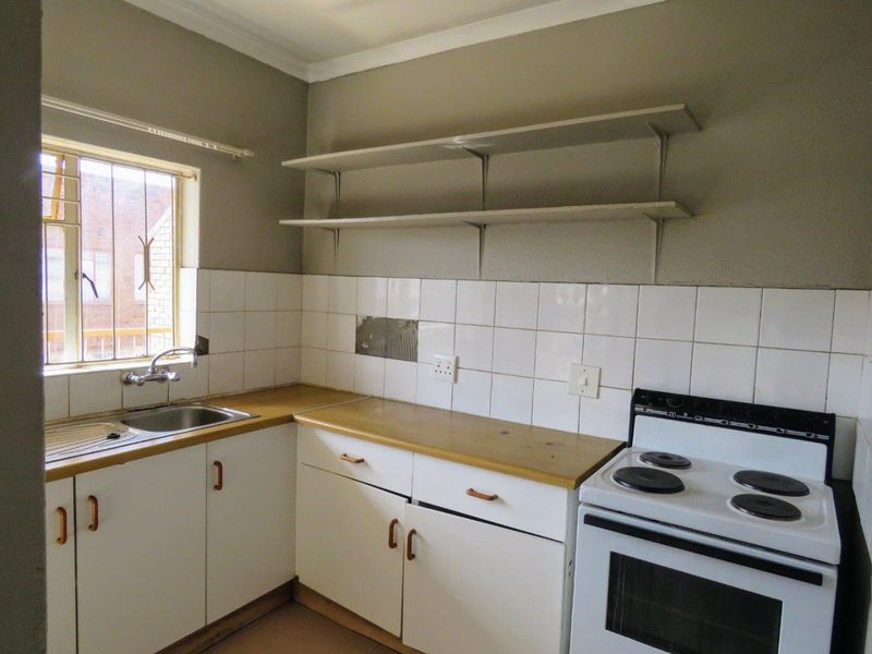 A functional kitchen featuring white cabinetry, laminate countertops, a tiled backsplash, and a freestanding stove, ready for modernization and cosmetic updates.