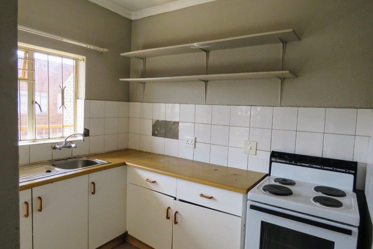 A functional kitchen featuring white cabinetry, laminate countertops, a tiled backsplash, and a freestanding stove, ready for modernization and cosmetic updates.