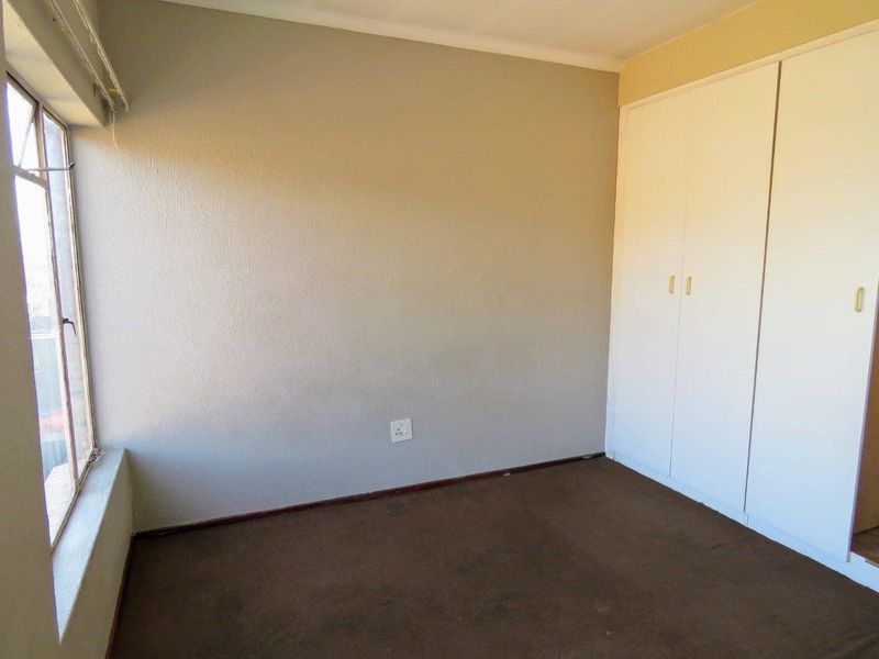 An empty bedroom featuring built-in cupboards, carpeted flooring, and a large window providing natural light.