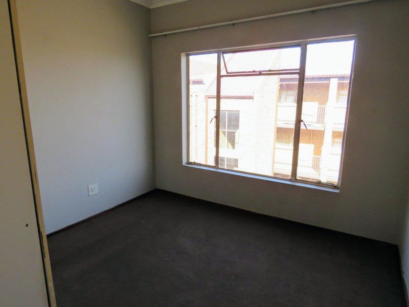 An empty bedroom featuring dark carpet flooring and a large window with a curtain rail, offering a blank canvas for personalization.