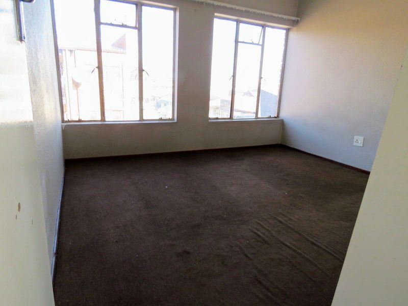 An empty bedroom featuring large windows that provide ample natural light and dark carpet flooring throughout.