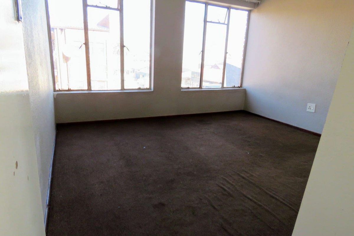 An empty bedroom featuring large windows that provide ample natural light and dark carpet flooring throughout.