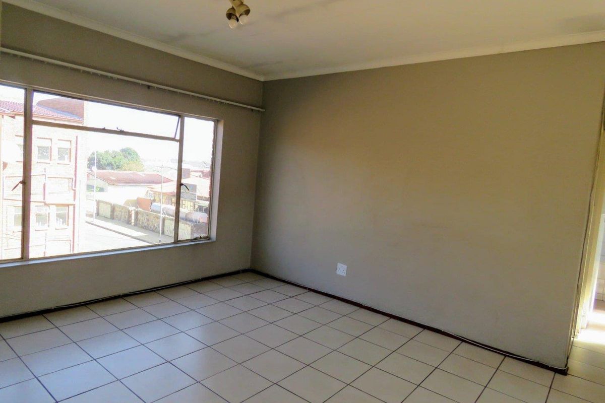 An empty living room featuring tiled flooring, neutral wall paint, and a large window providing natural light and an urban view.