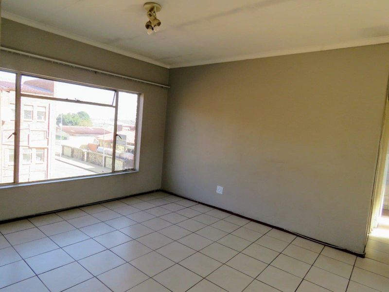 An empty living room featuring tiled flooring, neutral wall paint, and a large window providing natural light and an urban view.