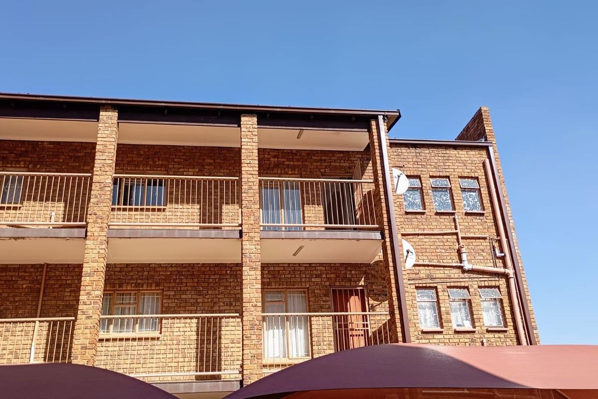 Exterior view of a multi-story apartment building featuring face brick construction, metal balcony railings, and multiple window units.