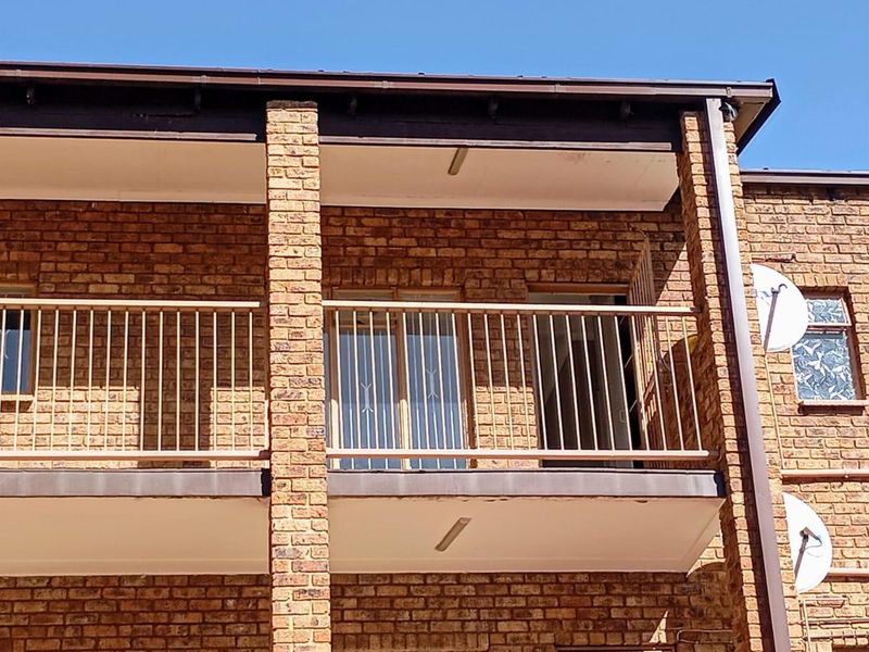 A view of an apartment balcony featuring brick exterior walls, metal railings, and sliding glass door access.
