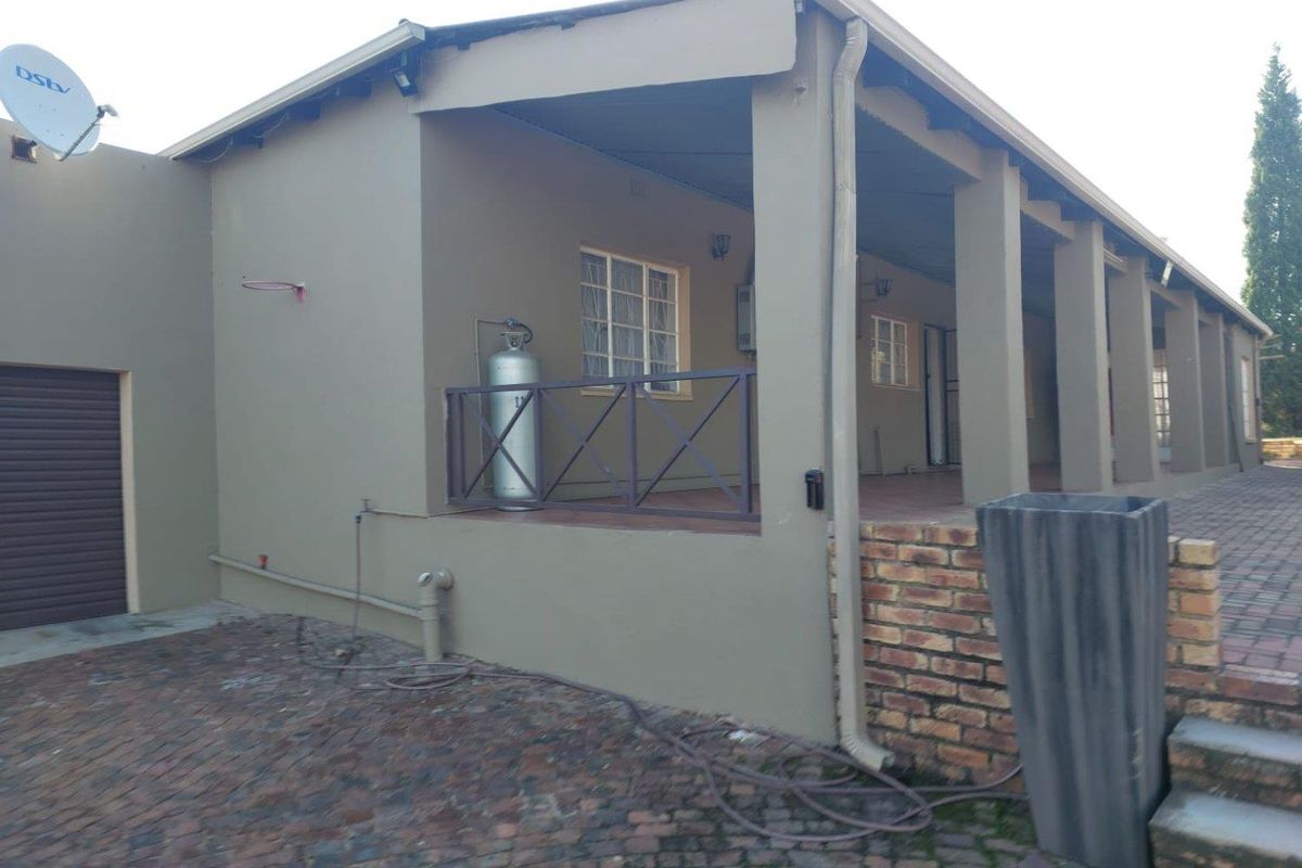 A view of the rear exterior of the farm property, featuring a covered patio area, brick paving, and a garage entrance.