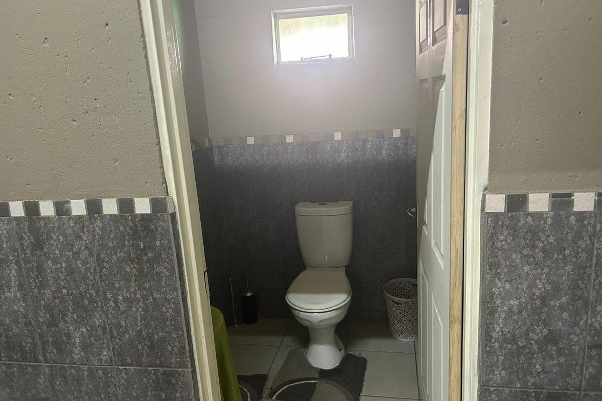 A compact bathroom featuring a standard toilet, tiled walls with a decorative border, and a small high-level window for ventilation.