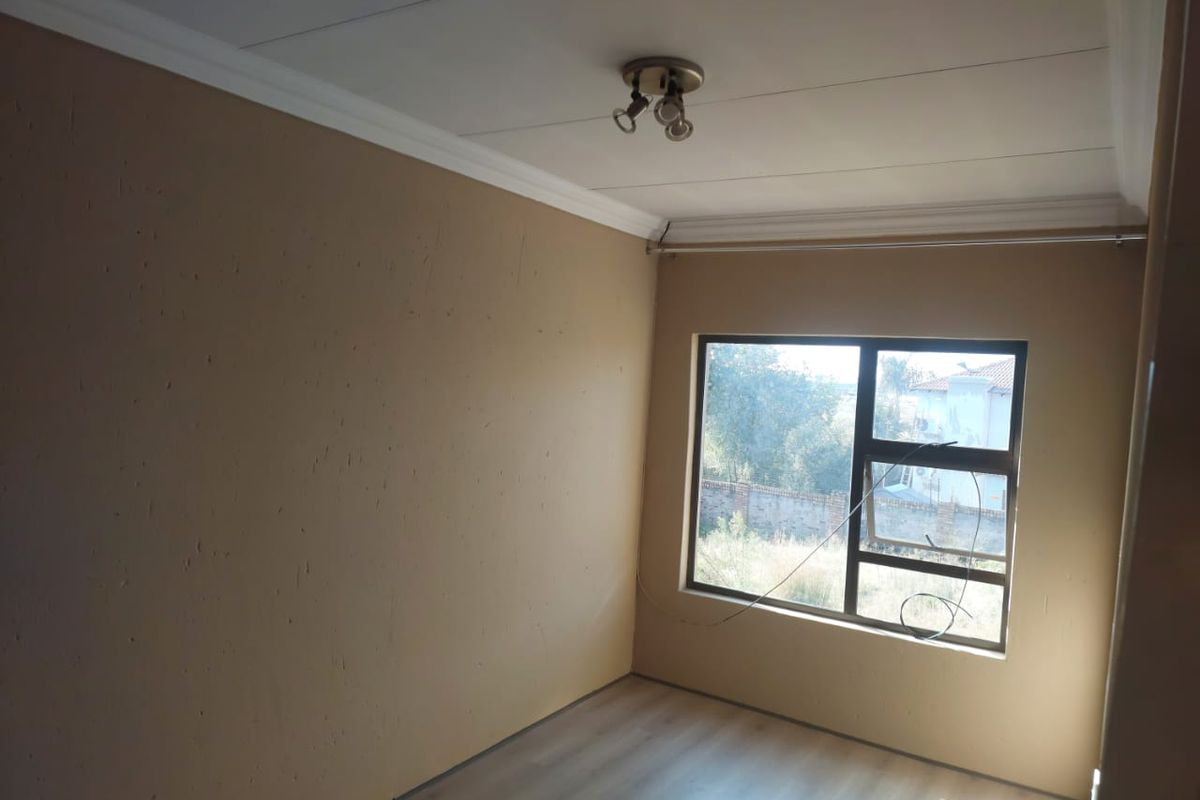 A vacant bedroom featuring light wood-look flooring, neutral painted walls, crown molding, and a large window with natural light.