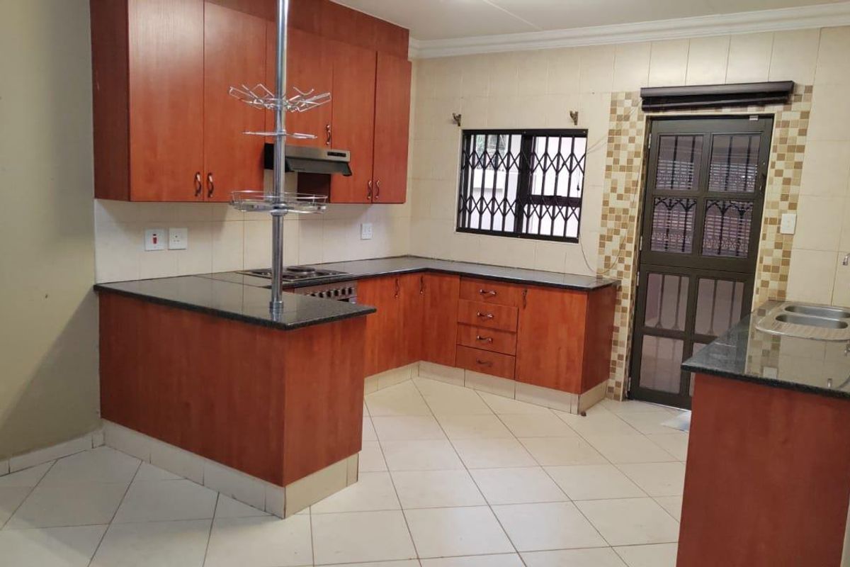 A functional kitchen featuring wood-finish cabinetry, granite countertops, a built-in hob, and an integrated extractor fan with direct access to the exterior.
