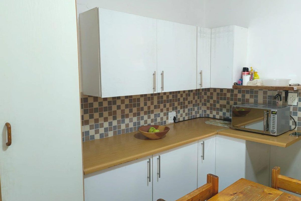 A functional kitchen area featuring white cabinetry, wood-look laminate countertops, and a mosaic tile backsplash.