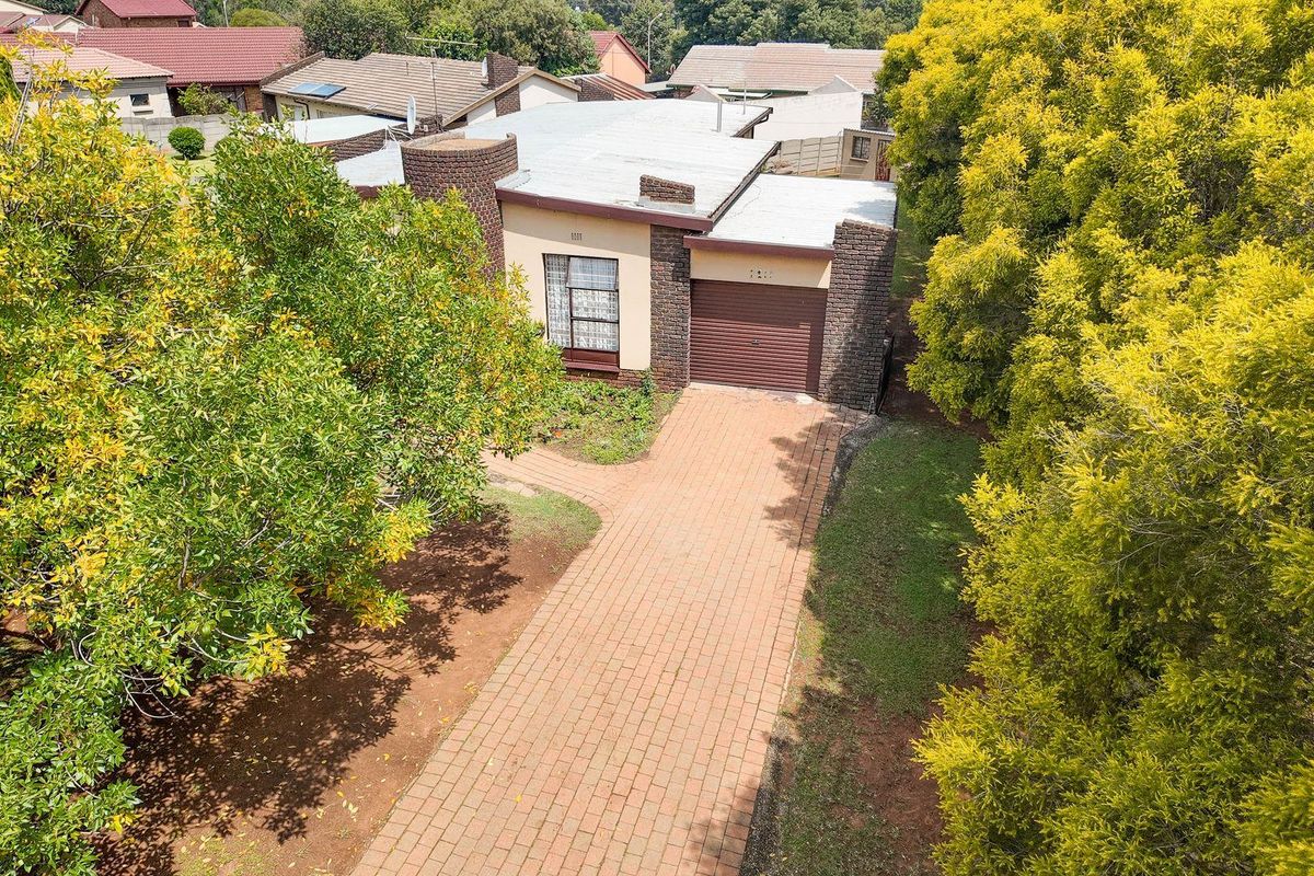 Aerial view of a single-story residential house featuring a paved driveway, attached garage, and established garden surroundings.