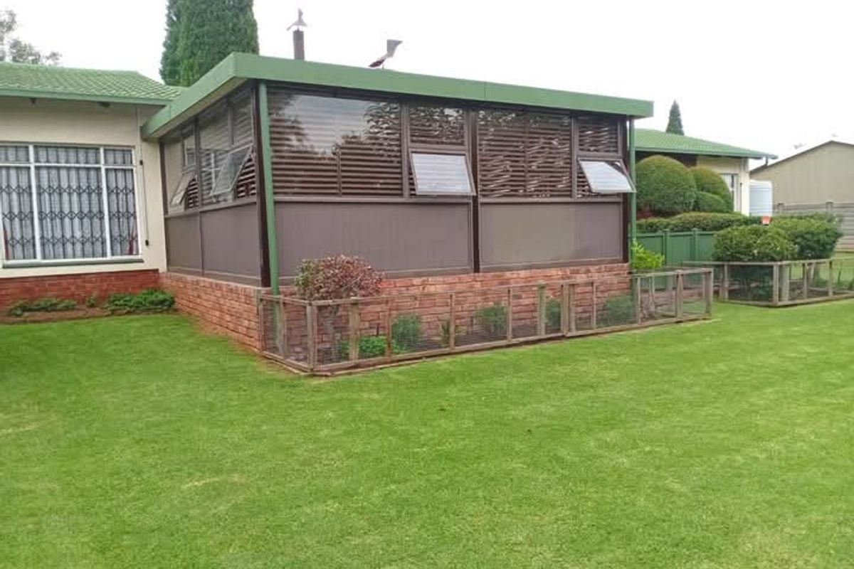 Rear view of the house featuring an enclosed patio area with brick foundation, security bars on windows, and a well-maintained lawn.