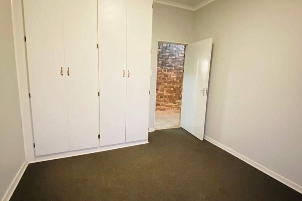 A clean, empty bedroom featuring neutral walls, dark carpeting, and ample built-in cupboard storage space.
