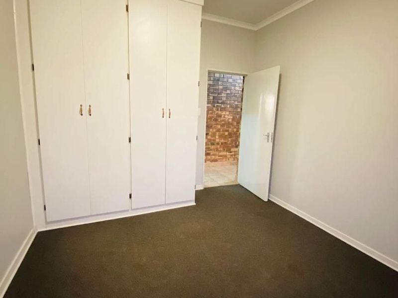 A clean, empty bedroom featuring neutral walls, dark carpeting, and ample built-in cupboard storage space.