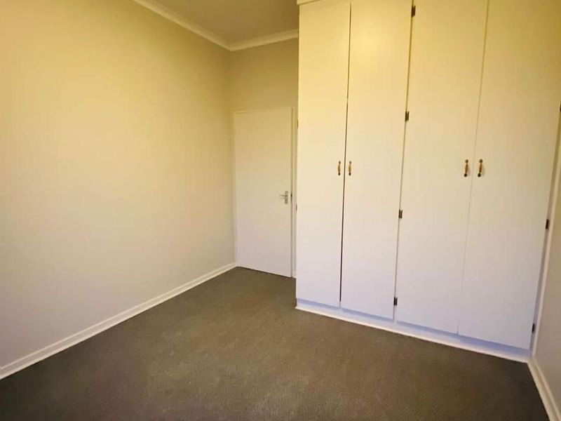 A clean, empty bedroom featuring neutral walls, carpeted flooring, and ample built-in cupboard storage space.