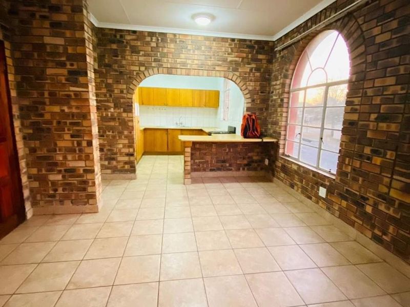Open plan living area featuring exposed brick walls, arched architectural details, ceramic tile flooring, and a breakfast bar connecting to the kitchen.