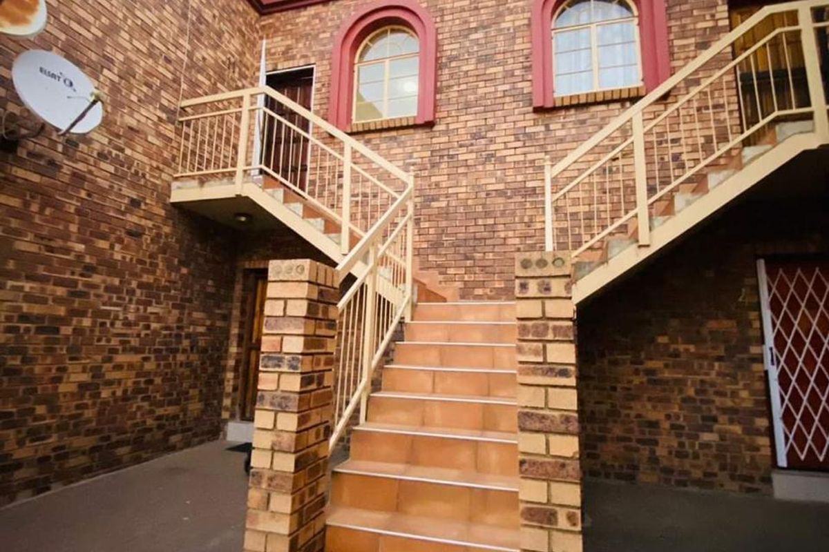 Exterior view of an apartment complex courtyard featuring a central brick staircase, metal balustrades, and arched windows on the upper level.