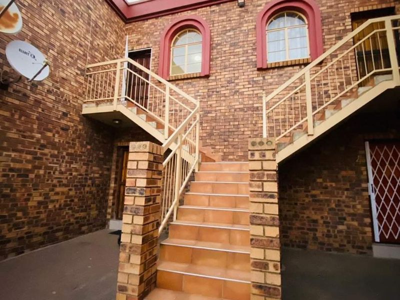 Exterior view of an apartment complex courtyard featuring a central brick staircase, metal balustrades, and arched windows on the upper level.