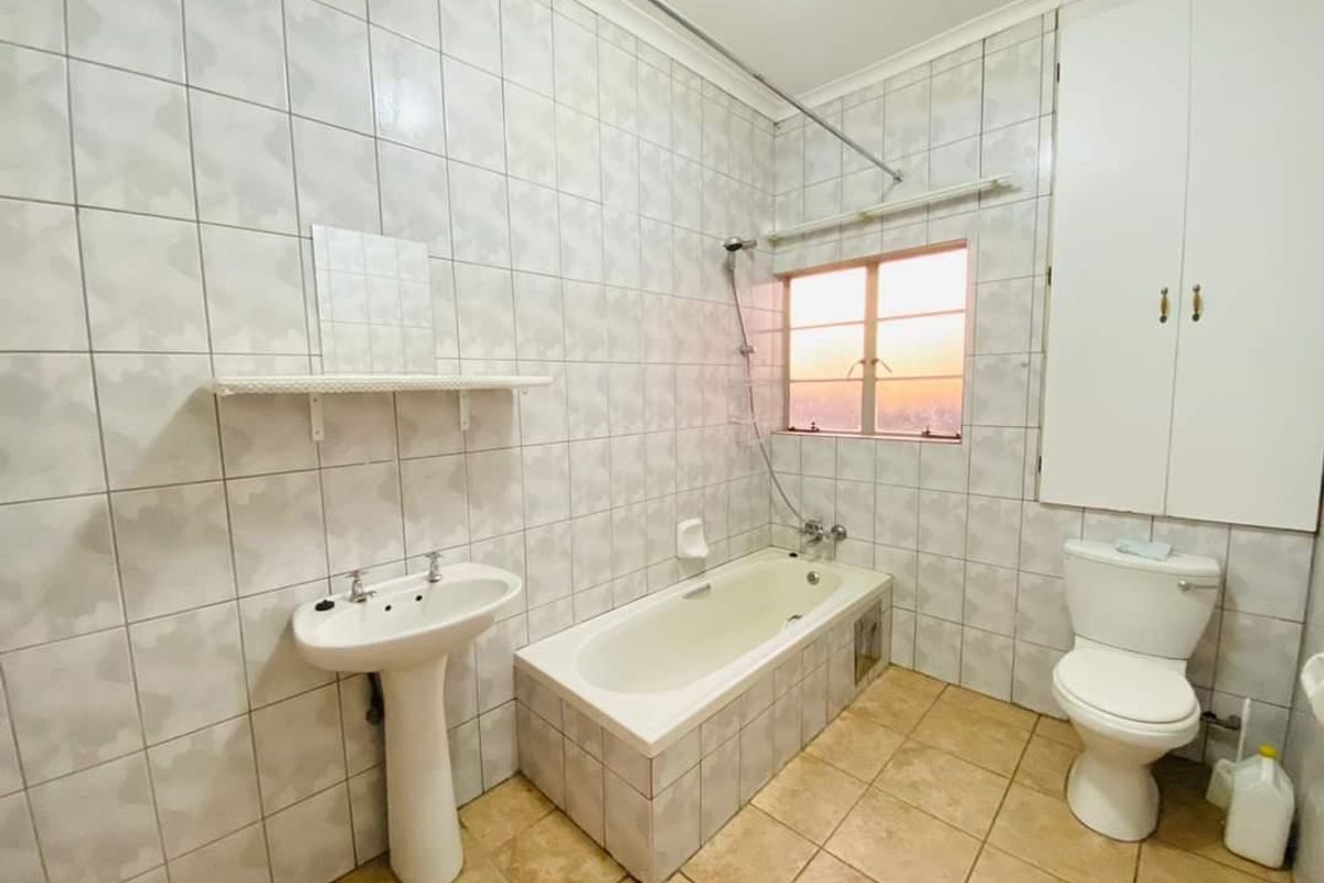 A functional bathroom featuring a pedestal basin, built-in bathtub with shower mixer, toilet, and integrated storage cupboard, finished with tiled walls and flooring.