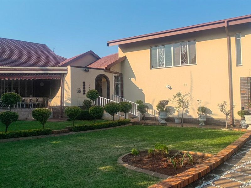 A well-maintained rear exterior view of the house featuring a covered patio, landscaped garden, and paved driveway area.