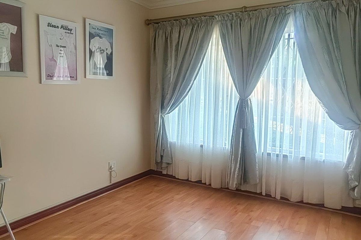 A bedroom featuring laminate flooring and a large window with curtains, providing a neutral space ready for personalization.