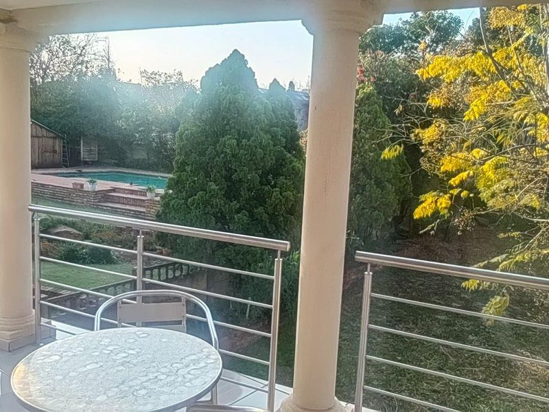 Covered balcony featuring a stainless steel balustrade and tiled flooring, overlooking the garden and swimming pool area.