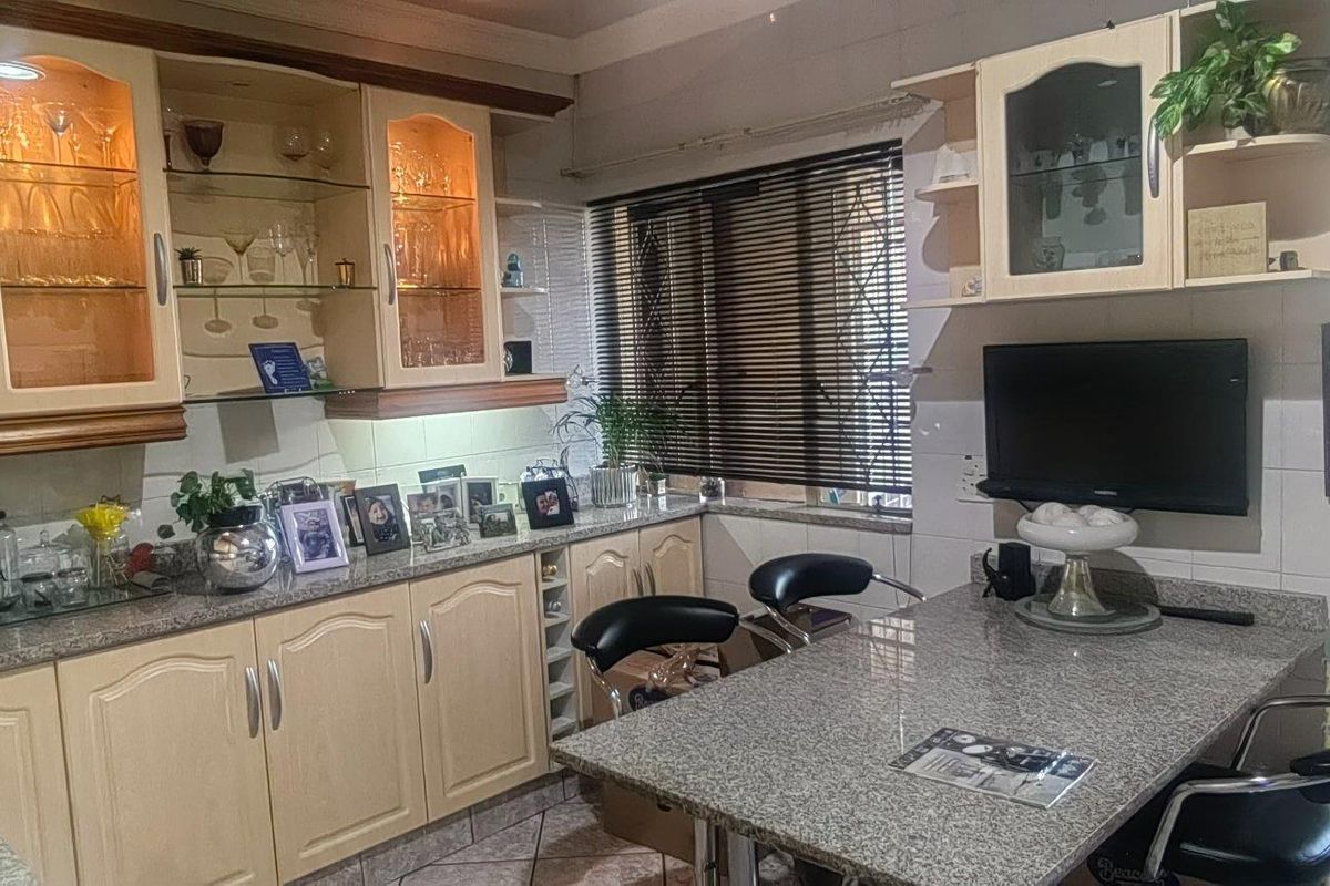 A functional kitchen featuring granite countertops, ample built-in cabinetry with glass-front display sections, under-cabinet lighting, and tiled flooring.