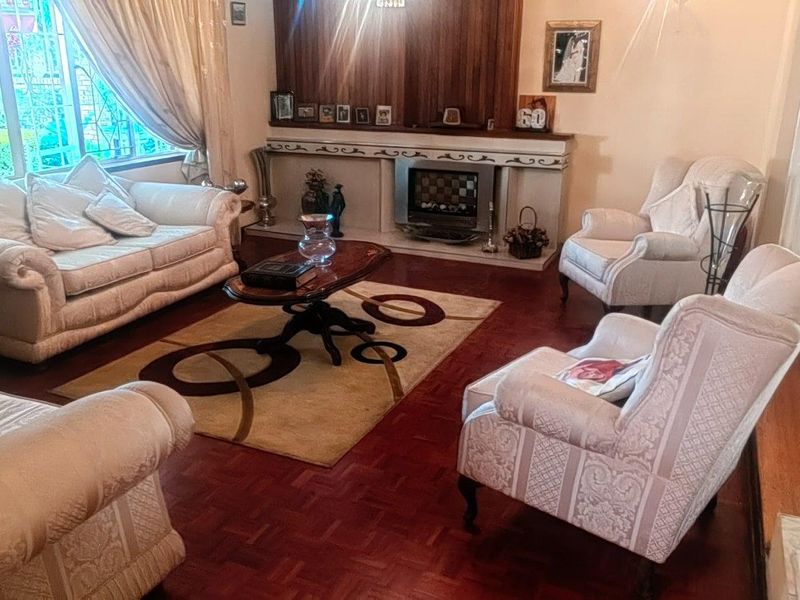 A traditional living room featuring warm parquet flooring, a built-in fireplace with a wooden mantel, and large windows allowing for natural light.