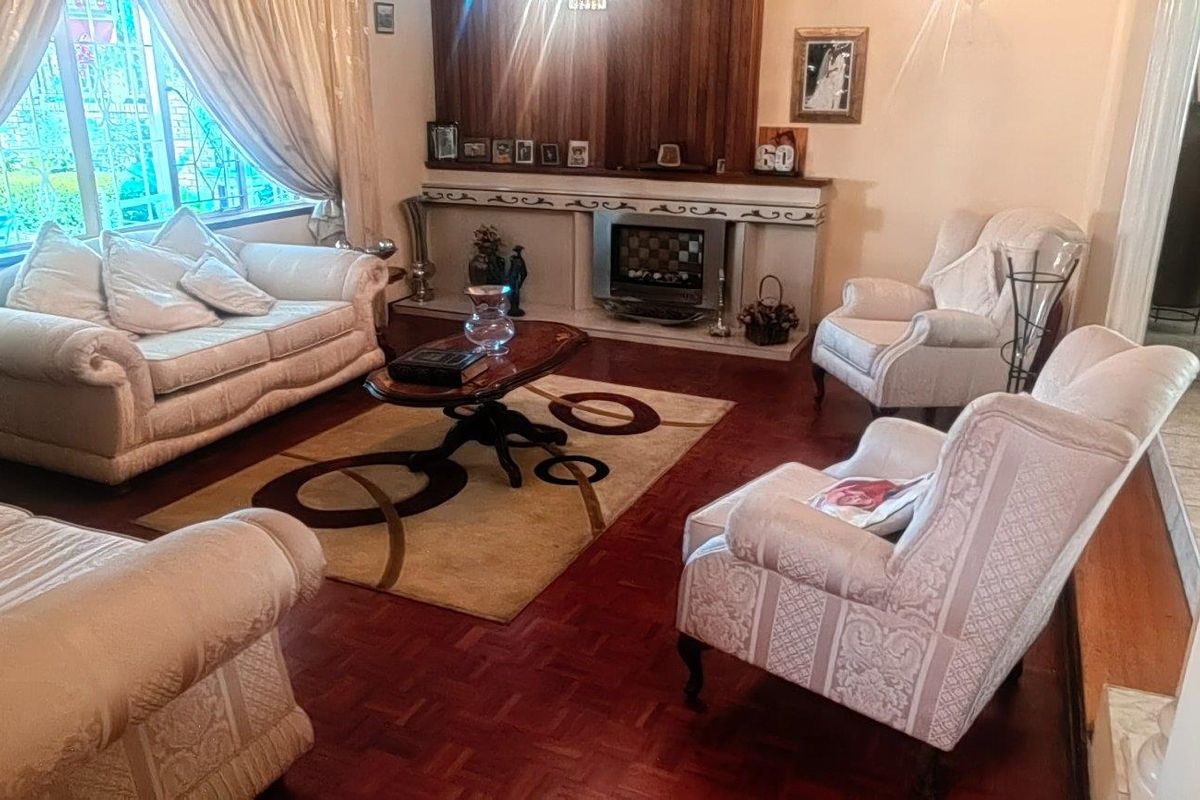 A traditional living room featuring warm parquet flooring, a built-in fireplace with a wooden mantel, and large windows allowing for natural light.