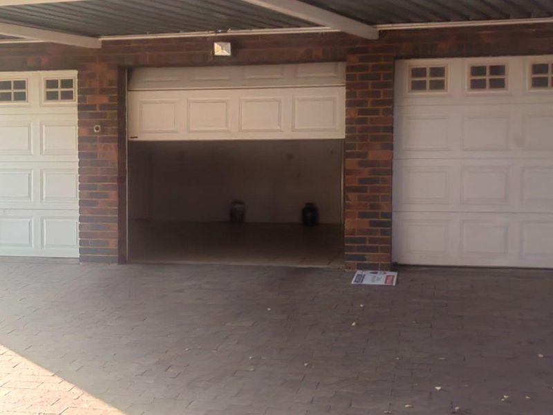 A triple garage featuring white panelled doors, brick exterior walls, and a paved driveway under a covered carport structure.