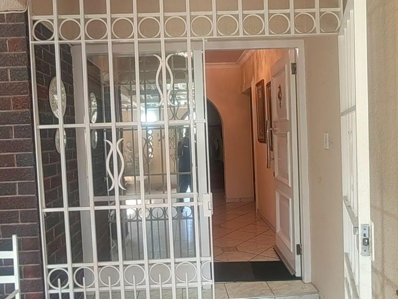 Entrance area featuring a white security gate, brick exterior wall, and tiled flooring leading into the home's interior hallway.