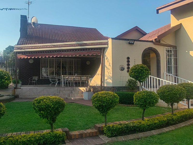 A well-maintained rear exterior view featuring a paved patio with a retractable awning, overlooking a manicured garden with established topiary shrubs.
