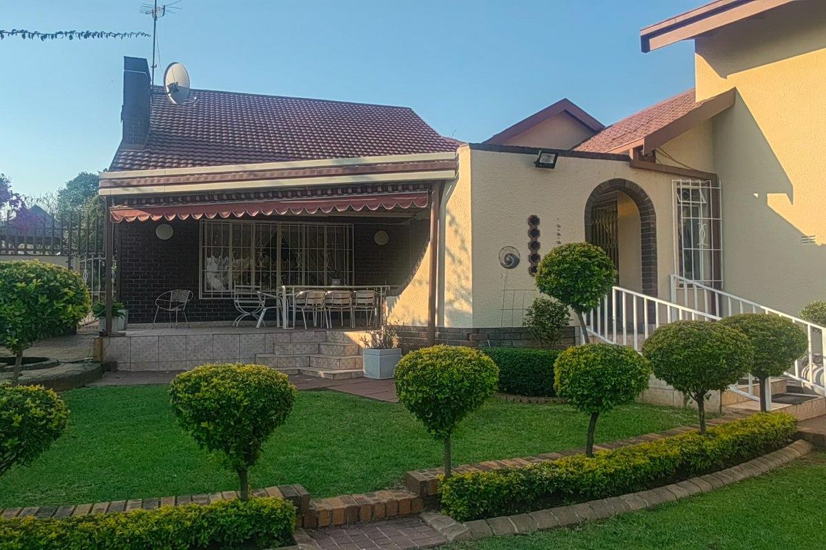 A well-maintained rear exterior view featuring a paved patio with a retractable awning, overlooking a manicured garden with established topiary shrubs.