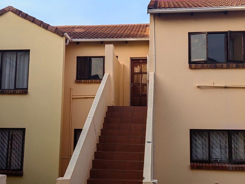 Exterior view of an apartment building featuring a tiled staircase leading to an upper-level entrance, with terracotta roof tiles and security-barred windows.