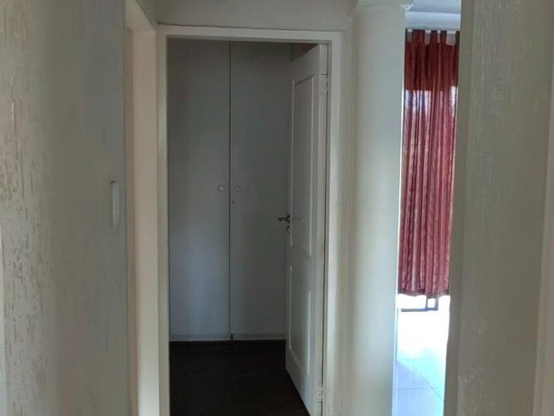 A functional hallway featuring tiled flooring, built-in storage cupboards, and decorative ceiling molding, leading towards an adjacent living area.