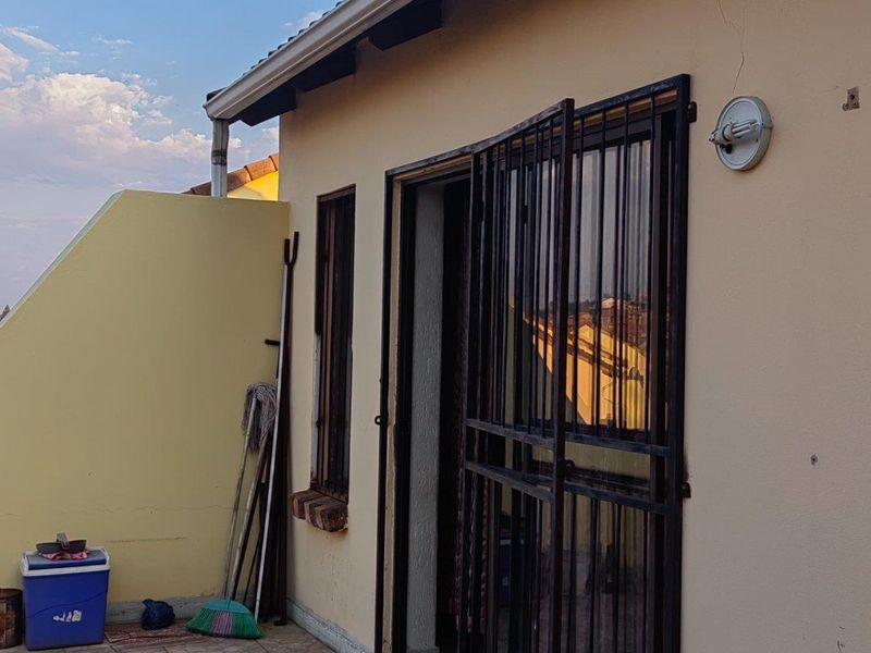 A balcony area featuring a security gate and exterior wall lighting, showing some signs of wear on the exterior plaster.