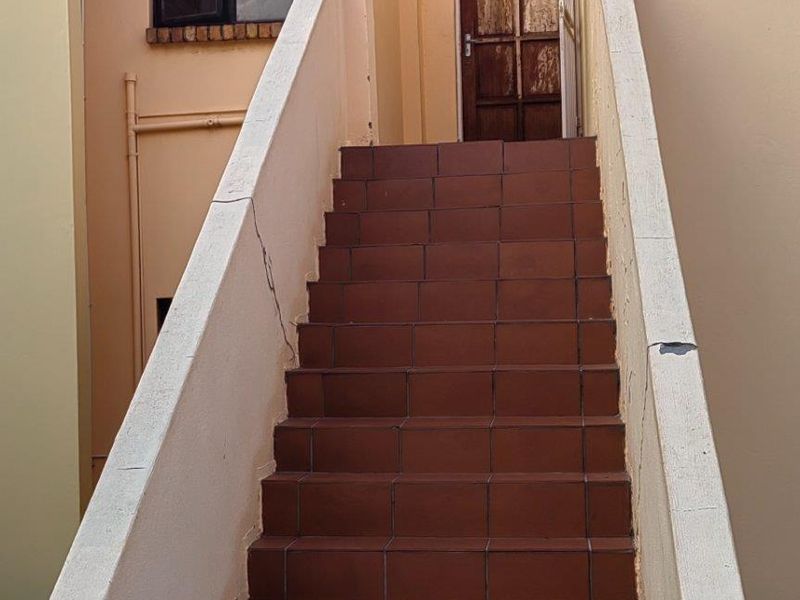 Exterior staircase leading to an apartment entrance, featuring tiled steps and a concrete balustrade showing signs of wear and weathering.