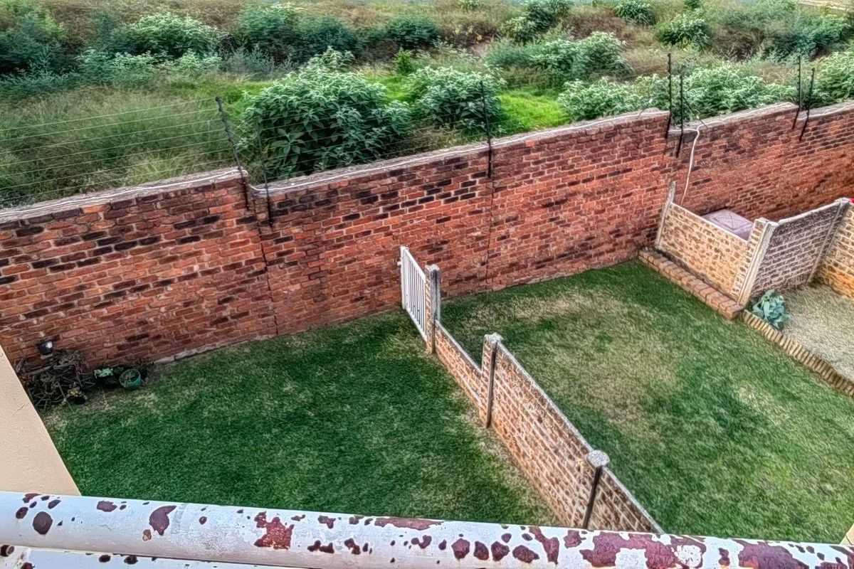 Elevated view of a private rear garden featuring a lawn, brick boundary walls with electric fencing, and a metal railing.