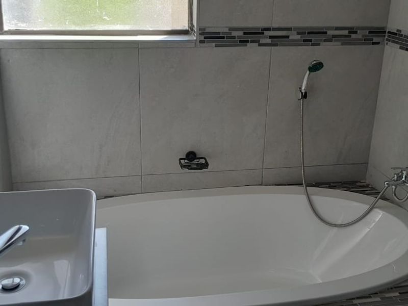 A modern bathroom featuring a white freestanding bathtub, a contemporary vessel sink with chrome fixtures, and neutral wall tiling with a decorative mosaic border.