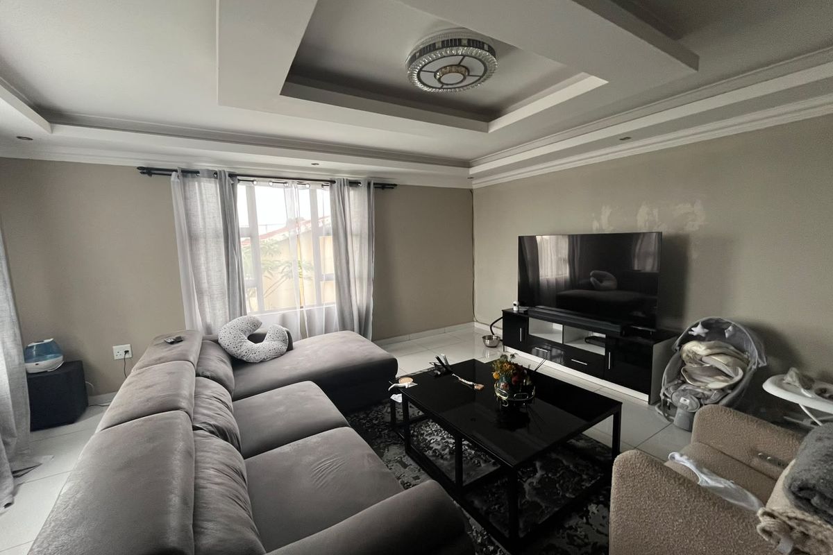 A living room featuring a recessed tray ceiling with cove lighting and tiled flooring, currently showing some minor wall surface imperfections.