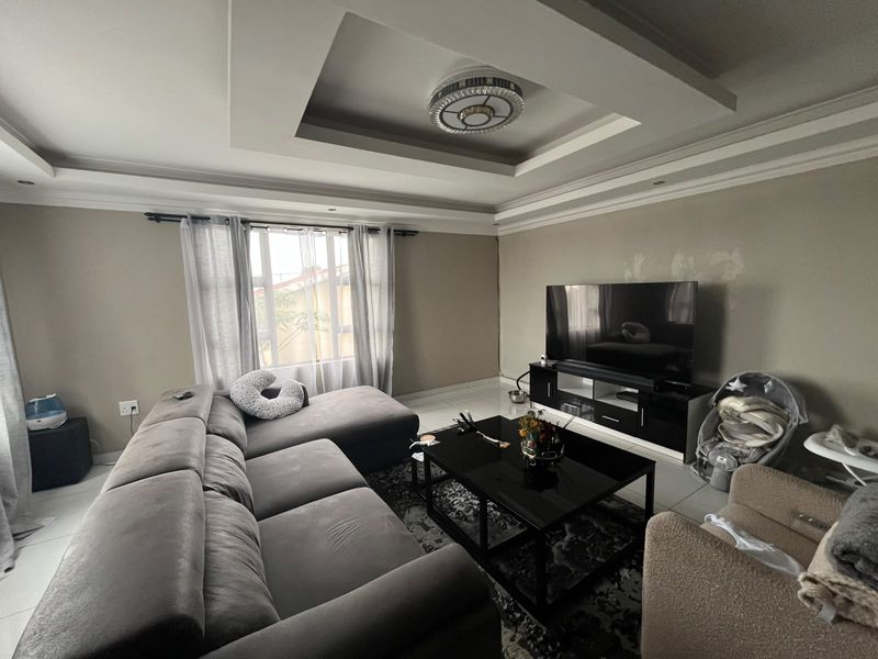A living room featuring a recessed tray ceiling with cove lighting and tiled flooring, currently showing some minor wall surface imperfections.