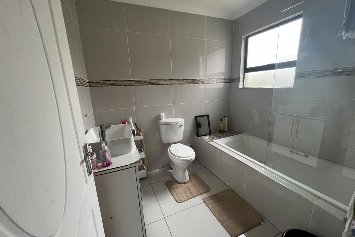A modern bathroom featuring a vessel sink vanity, a standard toilet, and a bathtub with a glass shower screen and neutral wall tiling.