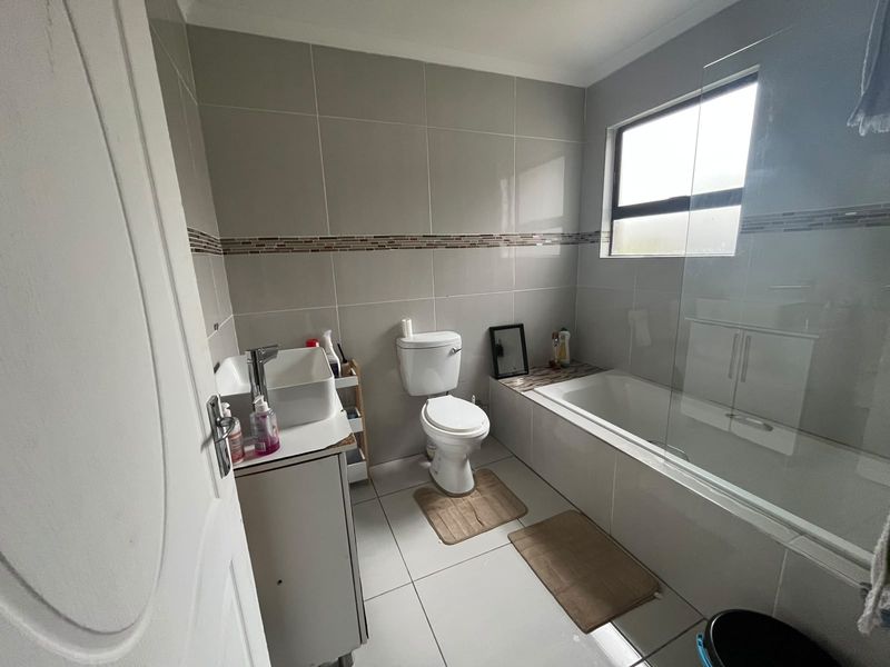 A modern bathroom featuring a vessel sink vanity, a standard toilet, and a bathtub with a glass shower screen and neutral wall tiling.