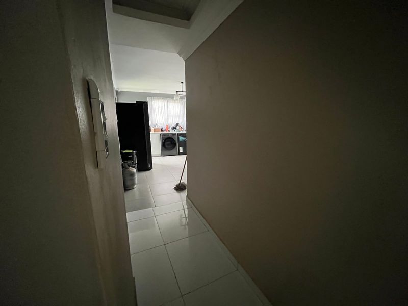 A view through a hallway leading into a kitchen area with tiled flooring and coved ceiling details.